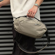 Male lifestyle shot of NIID NEO Nomad 5L Sling Bag‑N1L pearly gray textured crossbody sling bag, black adjustable shoulder strap, silver metal logo badge, urban metal shutter background, man holding top handle.