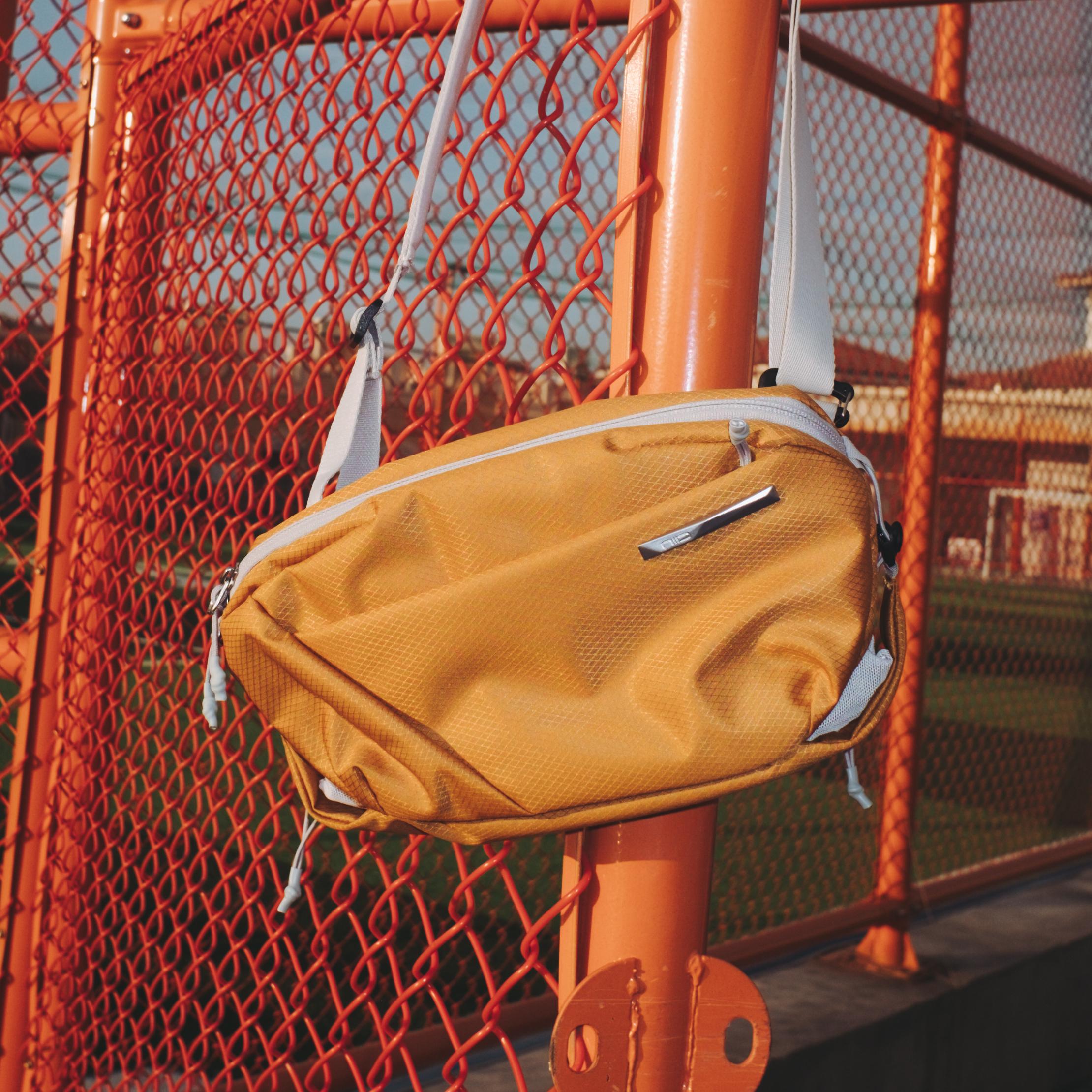 NIID NEO Nomad 4L Sling Bag in Amber Orange, real‑user outdoor lifestyle photo, displays textured water‑resistant fabric, silver metal hardware, white adjustable shoulder straps, compact cross‑body silhouette for daily commute, casual travel and street style.