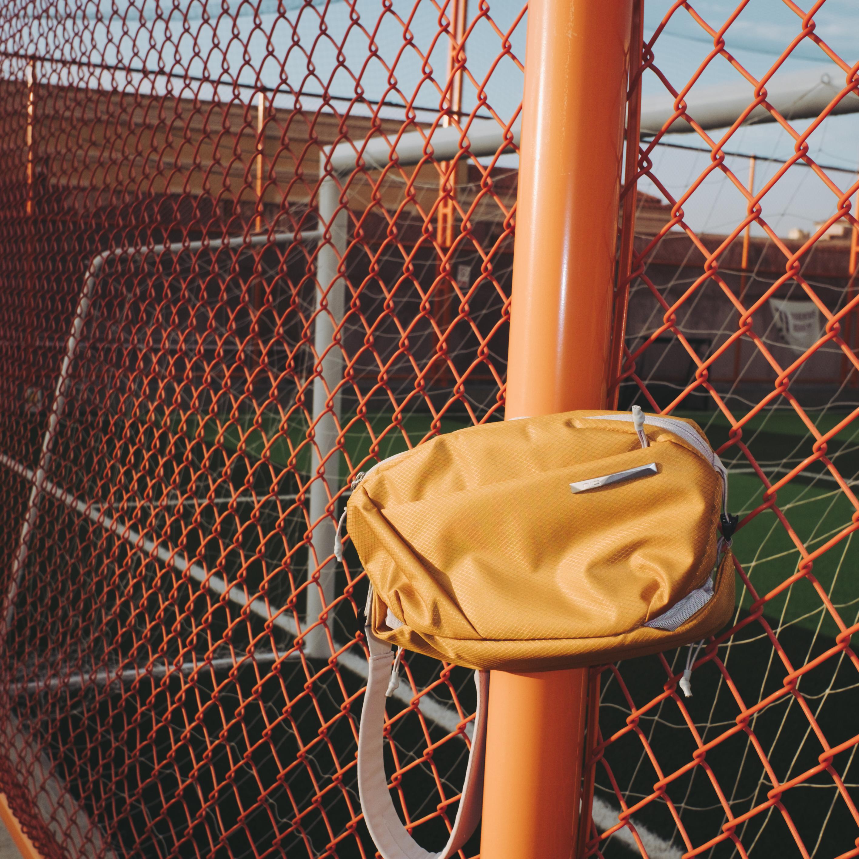 NIID NEO Nomad 4L Sling Bag in Amber Orange - Outdoor Sports Court Fence Lifestyle Display, Compact Waterproof Crossbody Bag for Casual Outings and Urban Commute