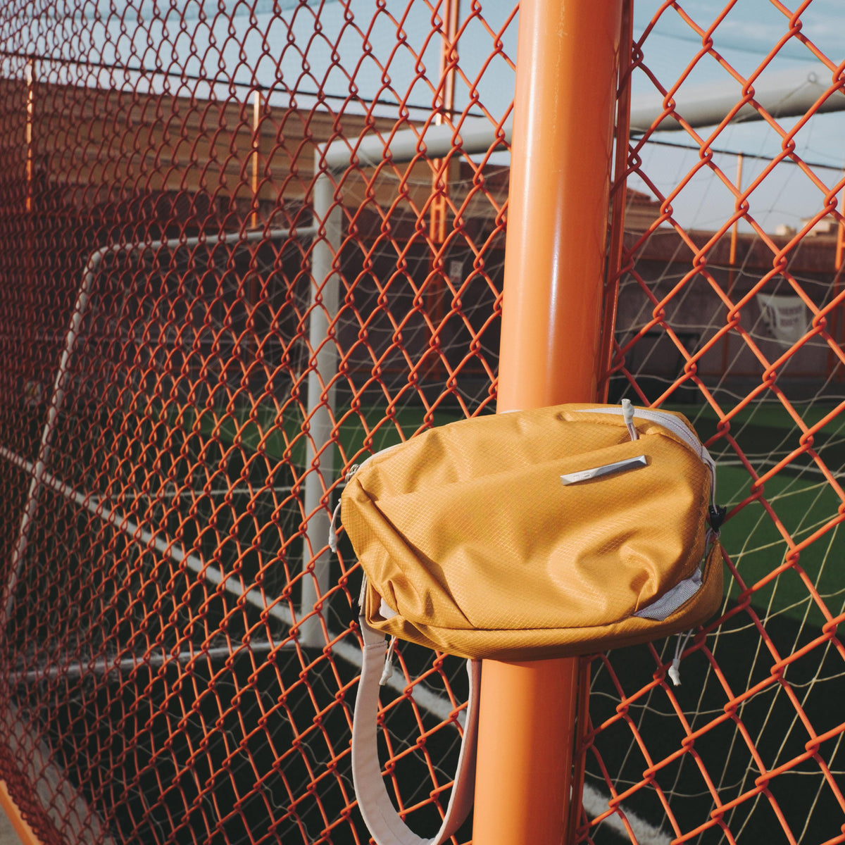 NIID NEO Nomad 4L Sling Bag in Amber Orange - Outdoor Sports Court Fence Lifestyle Display, Compact Waterproof Crossbody Bag for Casual Outings and Urban Commute