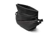 Three-quarter studio shot of Black Polyester NIID R1 Radiant Mega crossbody fanny sling bag with folded top flap opened, textured woven polyester fabric, front zipper pocket, engraved metal brand plate, adjustable woven shoulder strap buckles, isolated on plain white background