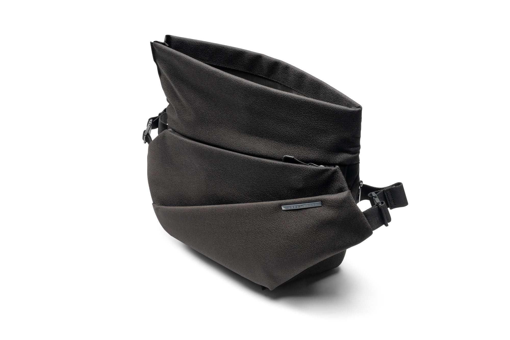 Three-quarter studio shot of Black Polyester NIID R1 Radiant Mega crossbody fanny sling bag with folded top flap opened, textured woven polyester fabric, front zipper pocket, engraved metal brand plate, adjustable woven shoulder strap buckles, isolated on plain white background