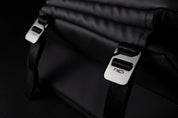 Dark background close-up of two engraved NIID silver metal buckles on meteorite black NIID R1 Radiant Urban Sling crossbody bag, thick woven nylon shoulder straps and folded waterproof nylon fabric, premium hardware detail shot highlighting durable adjustable fasteners for daily carry