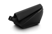 Side angle shot of meteorite black NIID R1 Radiant Urban Sling crossbody bag, waterproof nylon unisex anti-theft chest pack with adjustable shoulder strap and engraved metal brand plate, minimalist fold-over design on clean white background for daily commuting and travel