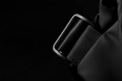 Dark moody close-up of textured plastic shoulder strap adjuster buckle on meteorite black NIID R1 Radiant Urban Sling crossbody bag, fine stitching on waterproof nylon strap, minimalist dark background highlighting hardware craftsmanship