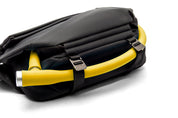 Close-up detail of meteorite black NIID R1 Radiant Urban Sling crossbody bag, bright yellow ergonomic padded shoulder strap with branded metal adjuster buckles, soft cushioned carrying design for long-time daily commute and outdoor travel, shot on clean white background