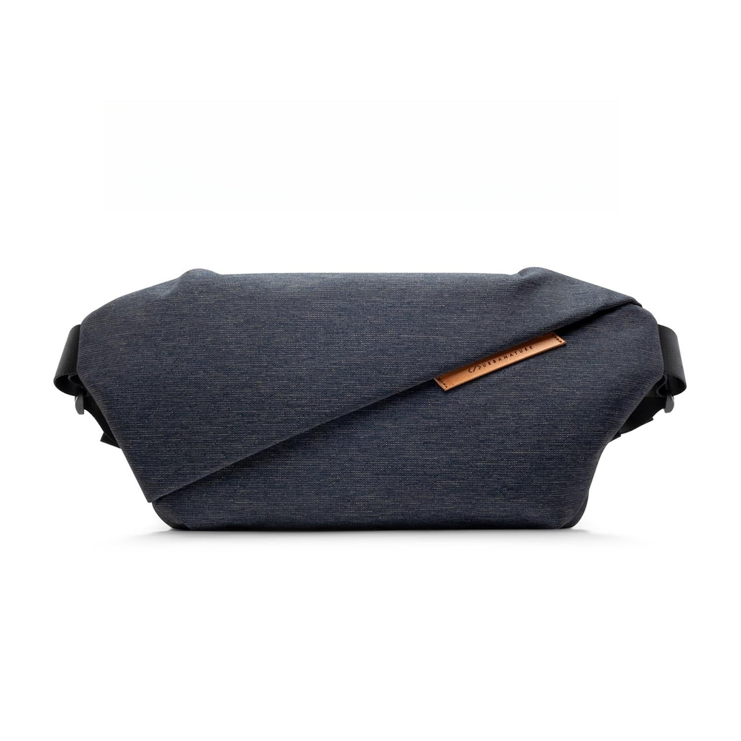 Front studio shot of Indigo NIID RO Plus Sling Bag, dark denim textured waterproof nylon crossbody chest fanny pack with diagonal fold design and genuine leather brand tag, adjustable full shoulder straps, clean 1:1 square white e-commerce product background for variant gallery