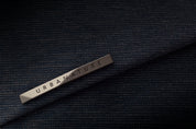 Close-up detail shot of metallic engraved URBANATURE brand tag laid on textured dark indigo woven waterproof bag fabric, premium material texture showcase