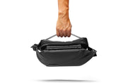 A hand holding black NIID RO Radiant crossbody chest bag with open multi-layer zipper compartments, isolated on clean white background