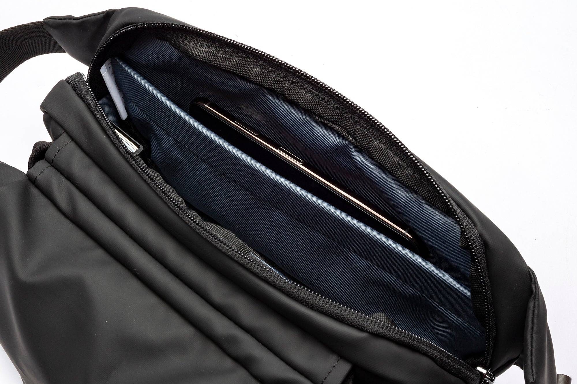 Close-up view of black NIID RO Radiant sling bag inner compartment, large padded slot holding smartphone, smooth dark blue lining and durable zipper