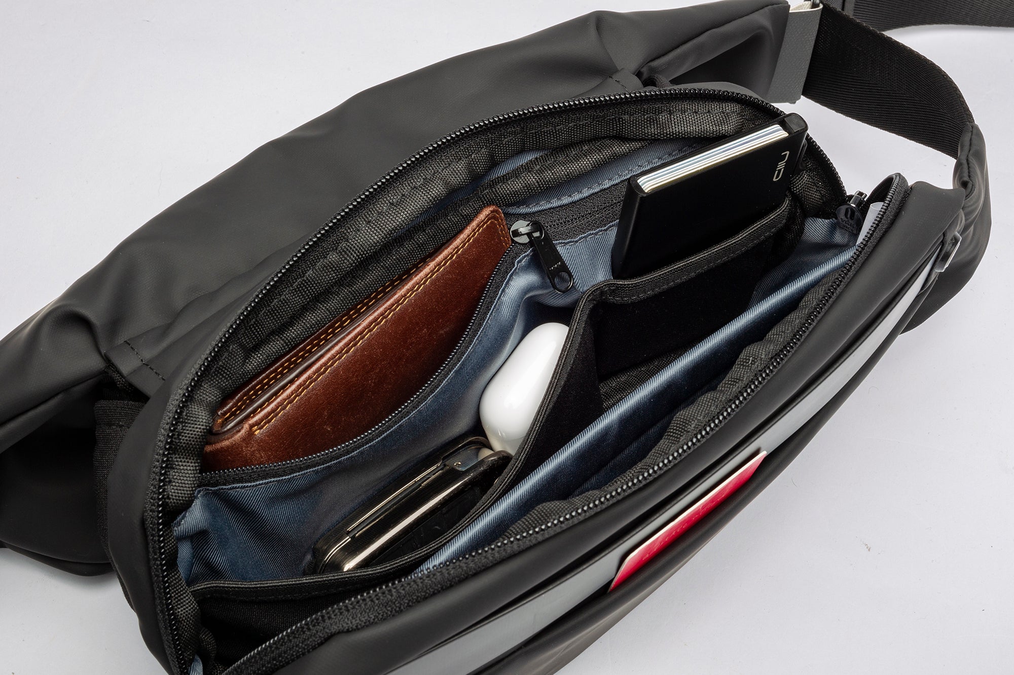 Close-up shot of open black NIID RO Radiant crossbody bag interior, multi-compartment organizer holding wallet, card holder and earbuds, demonstrating classified storage space