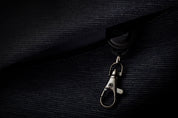Dark mood close-up of metallic lobster claw hook accessory attached to indigo textured woven bag fabric, premium hardware detail shot