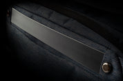 Moody close-up detail of indigo woven NIID RO sling bag side panel, featuring matte rubber trim, metal snap rivet and heavy-duty zipper on dark shadowed background