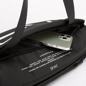 Close-up detail shot of black NIID S6 Hybrid Sling crossbody bag, front zipper pocket holding smartphone, printed NIID brand text and slogan fabric lining, dual top handles, plain white studio background