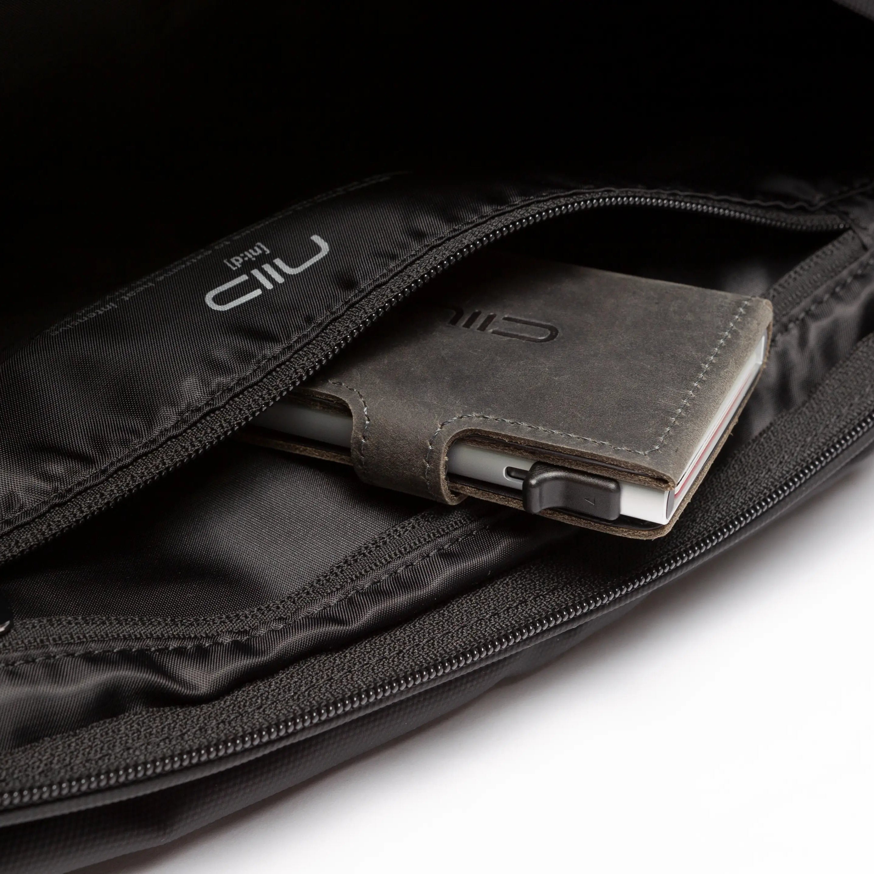 Close-up interior shot of black NIID S6 Hybrid Sling crossbody bag, zipper pocket storing leather wallet with smartphone, white NIID logo lining, clean white background