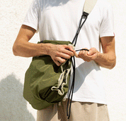 Close-up lifestyle detail shot of Khaki/Olive NIID ST@TEMENT S7 Tote Bag, male hands pulling the built-in drawstring closure, olive green lightweight fabric, matching drawstring toggle, adjustable mixed-texture shoulder strap detail, plain white textured wall background, showcase of the bag’s cinch feature