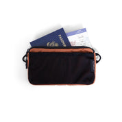 NIID NEO Element Pouch in black with Venetian Red lining, top-down shot holding passport and boarding pass, travel document organizer