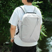 Back‑side shot of male model with NIID NEO Nomad 19L Backpack‑N3 glacier gray grid fabric, green bamboo waterside background, slim lightweight daypack for everyday commute and short trips.