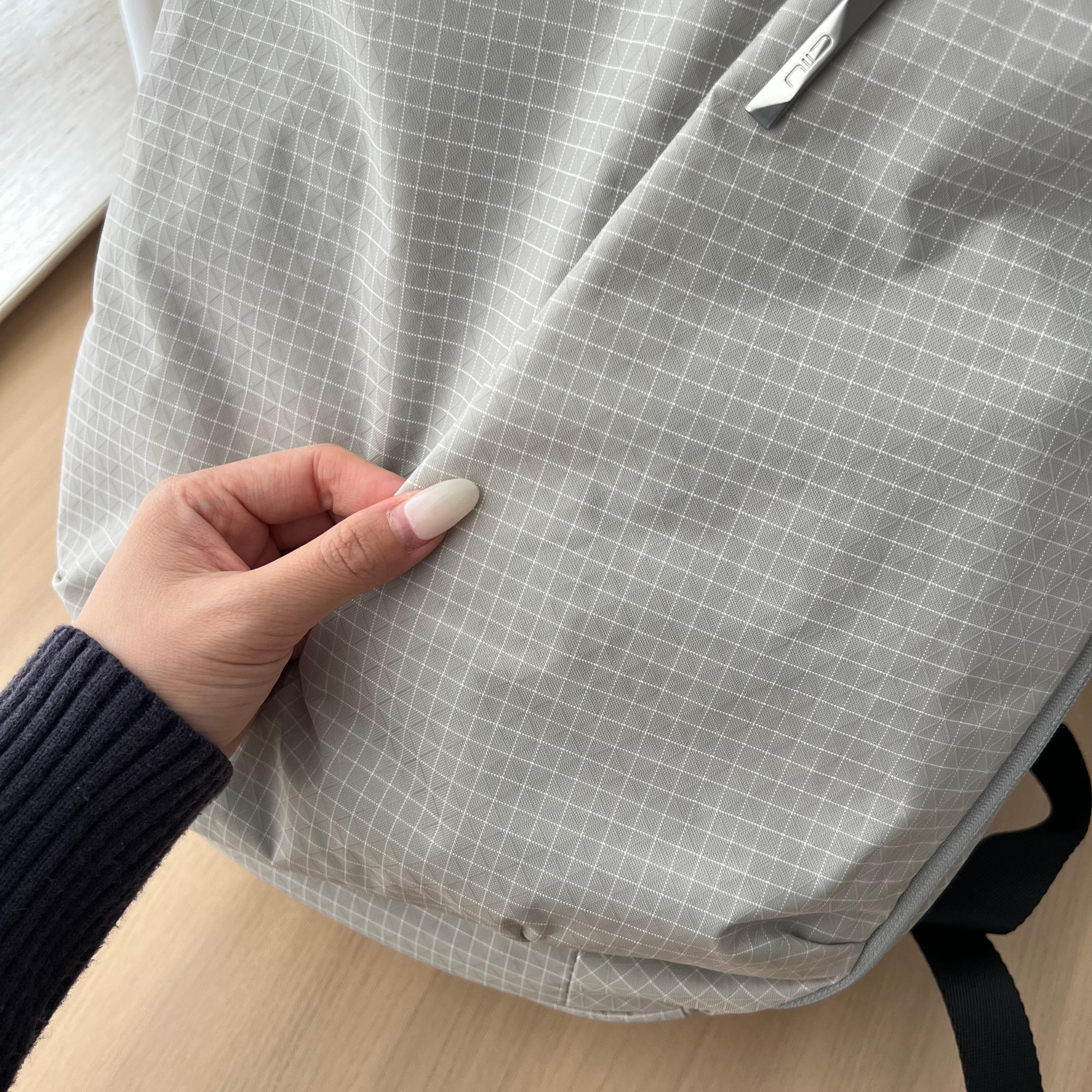Close‑up texture shot of NIID NEO Nomad 19L Backpack‑N3 glacier gray grid rip‑stop fabric, hand demonstrating soft flexible material, durable lightweight textile detail.