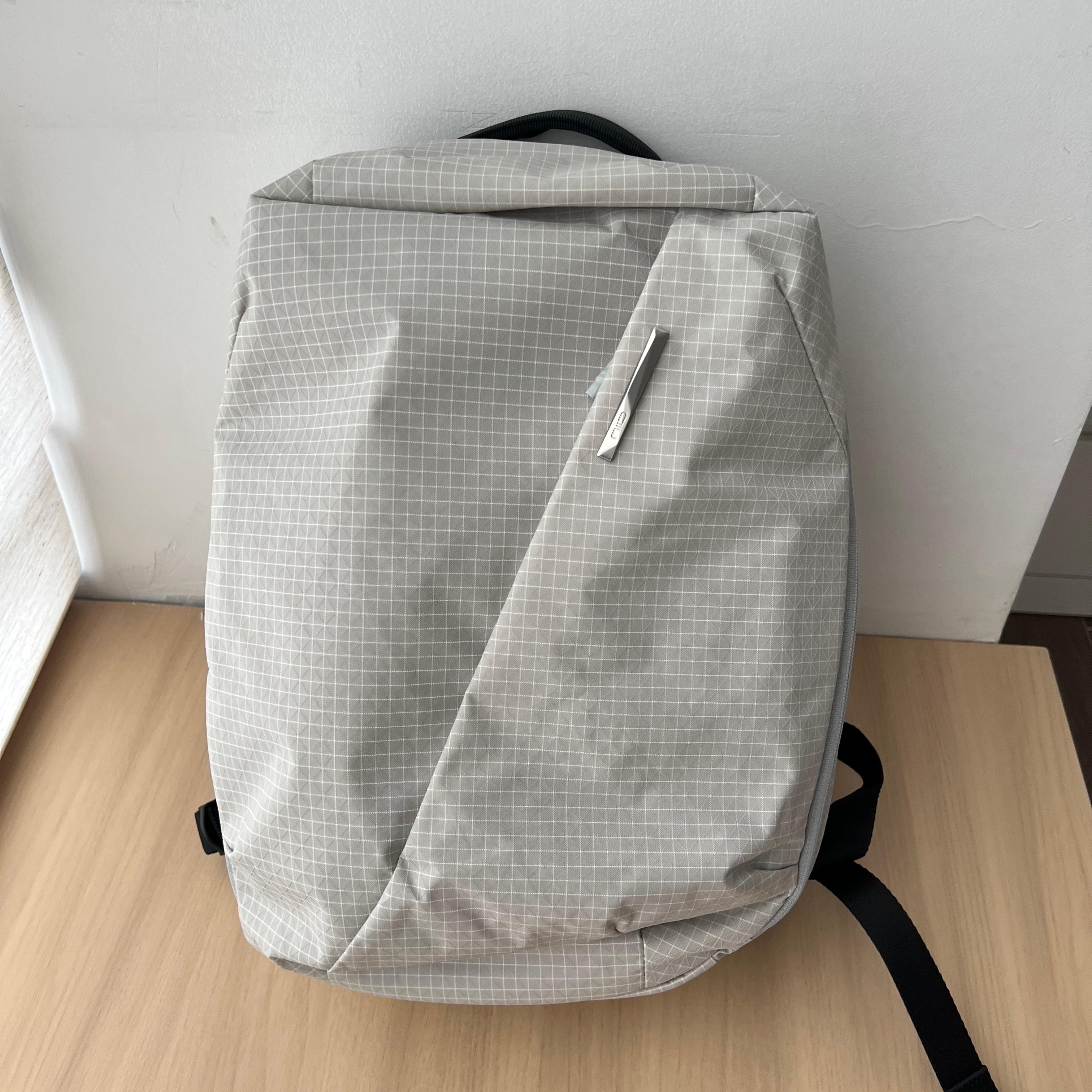 Studio indoor product shot of NIID NEO Nomad 19L Backpack‑N3 glacier gray grid fabric, placed on light wooden table against white wall, clean front view showing minimalist silhouette.