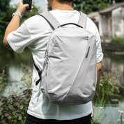 Back view of male model wearing NIID NEO Nomad 19L Backpack‑N3 glacier gray grid fabric, urban outdoor scene, lightweight water‑resistant daypack for city commute and casual travel.