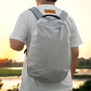 Back view of male model carrying NIID NEO Nomad 19L Backpack‑N3 glacier gray grid fabric at sunset riverside scene, lightweight water‑resistant daypack for urban travel and daily commute.