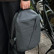 Urban lifestyle shot of NIID NEO Nomad Backpack‑N3 mineral gray, person holding top handle beside bicycle, side water bottle pocket displayed, for commute, cycling and daily city travel.