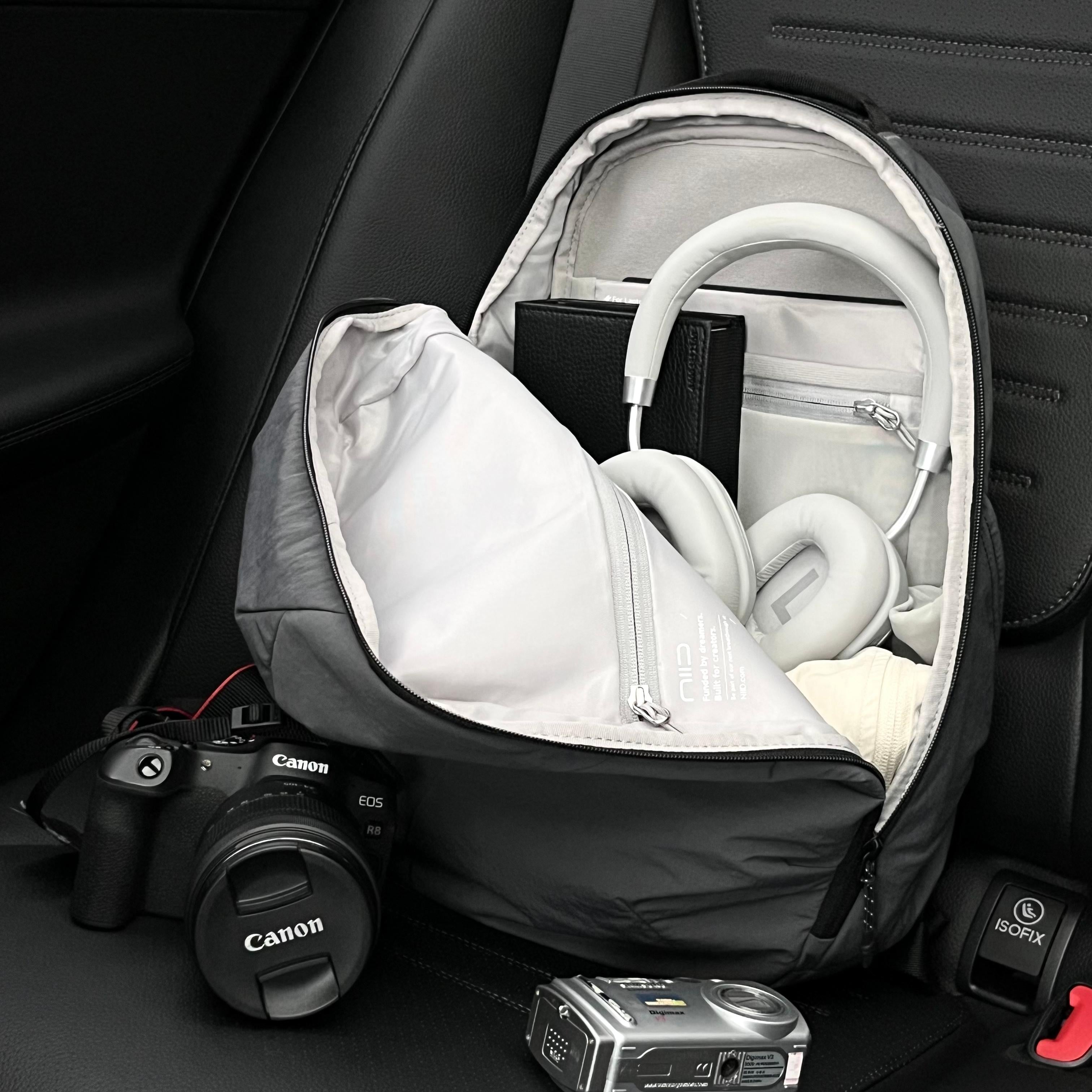 Car interior lifestyle shot of open NIID NEO Nomad 19L Backpack‑N3 mineral gray, displays inner compartment layout, packed with headphones, camera gear, showing ample storage space for travel and photography essentials.