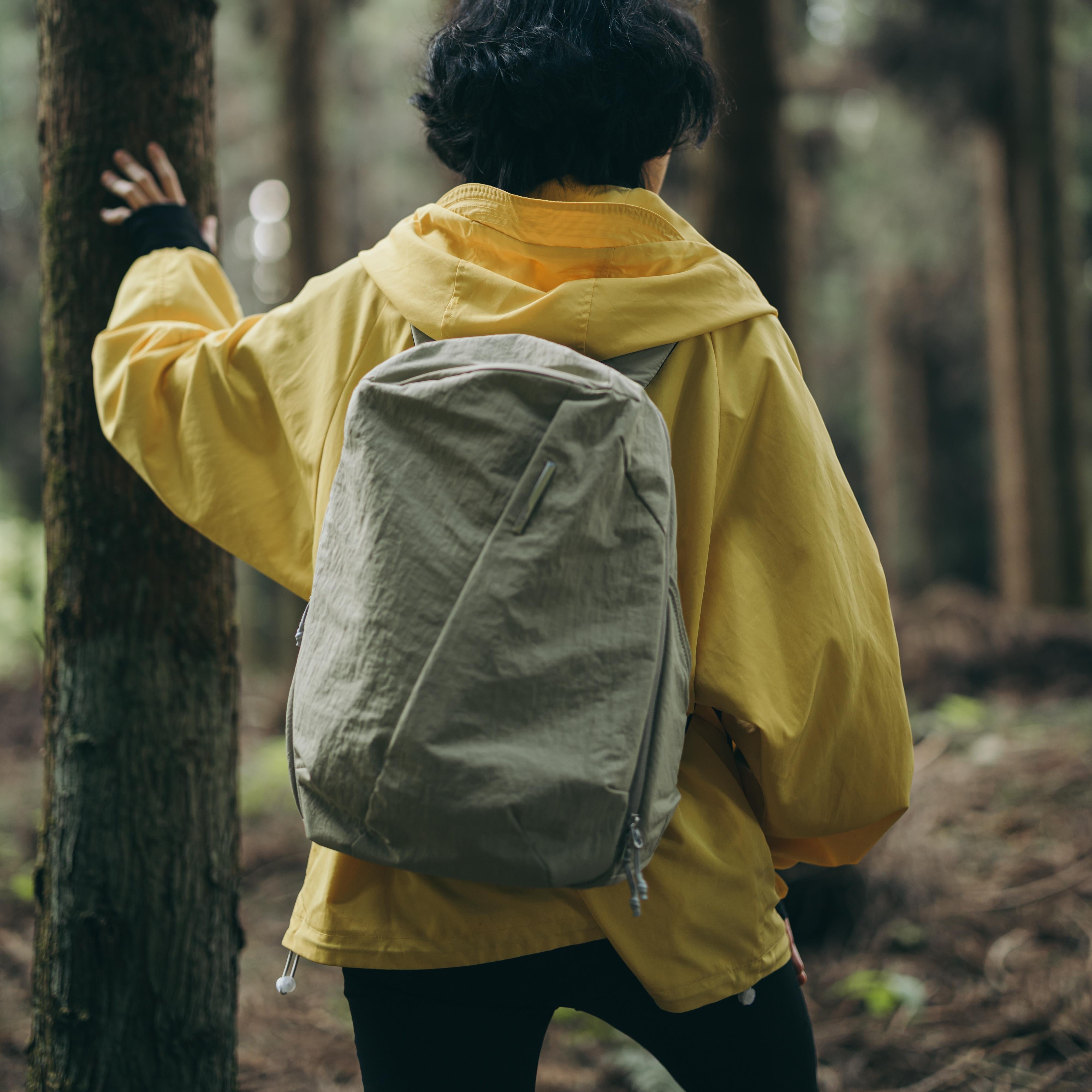 Back view of model wearing NIID NEO Nomad 19L Backpack‑N3 sage green in forest, lightweight water‑resistant daypack for hiking, casual outdoor adventure and weekend short travel.