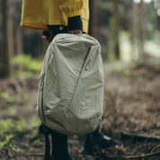 Hand‑held shot of NIID NEO Nomad 19L Backpack‑N3 sage green in woodland setting, textured water‑resistant fabric, minimalist daypack for outdoor hiking and weekend travel.