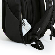 Close-up of NIID NEO Nomad Backpack N4 side zipper pocket holding smartphone, showing shoulder strap with NIID logo tag.