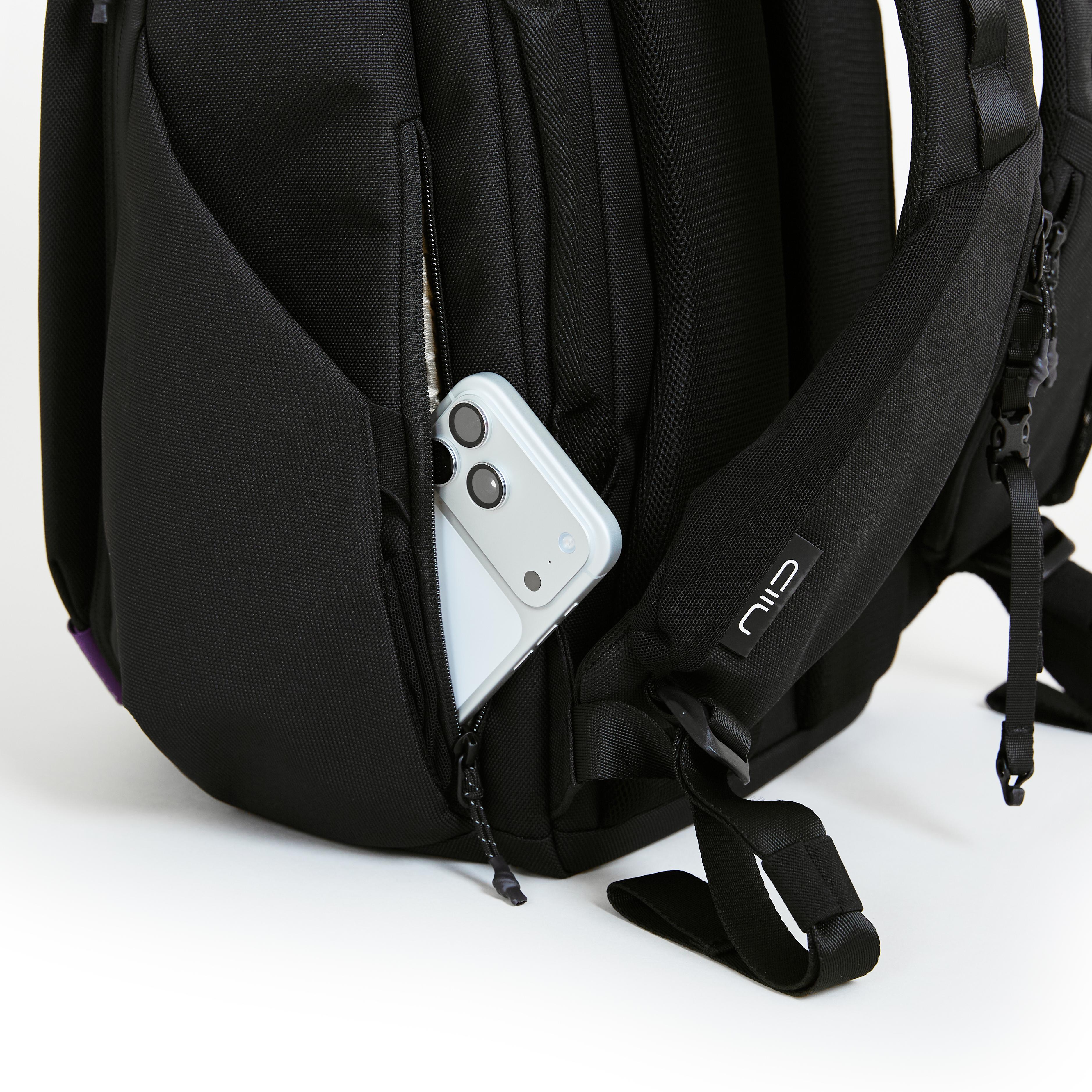 Close-up of NIID NEO Nomad Backpack N4 side zipper pocket holding smartphone, showing shoulder strap with NIID logo tag.