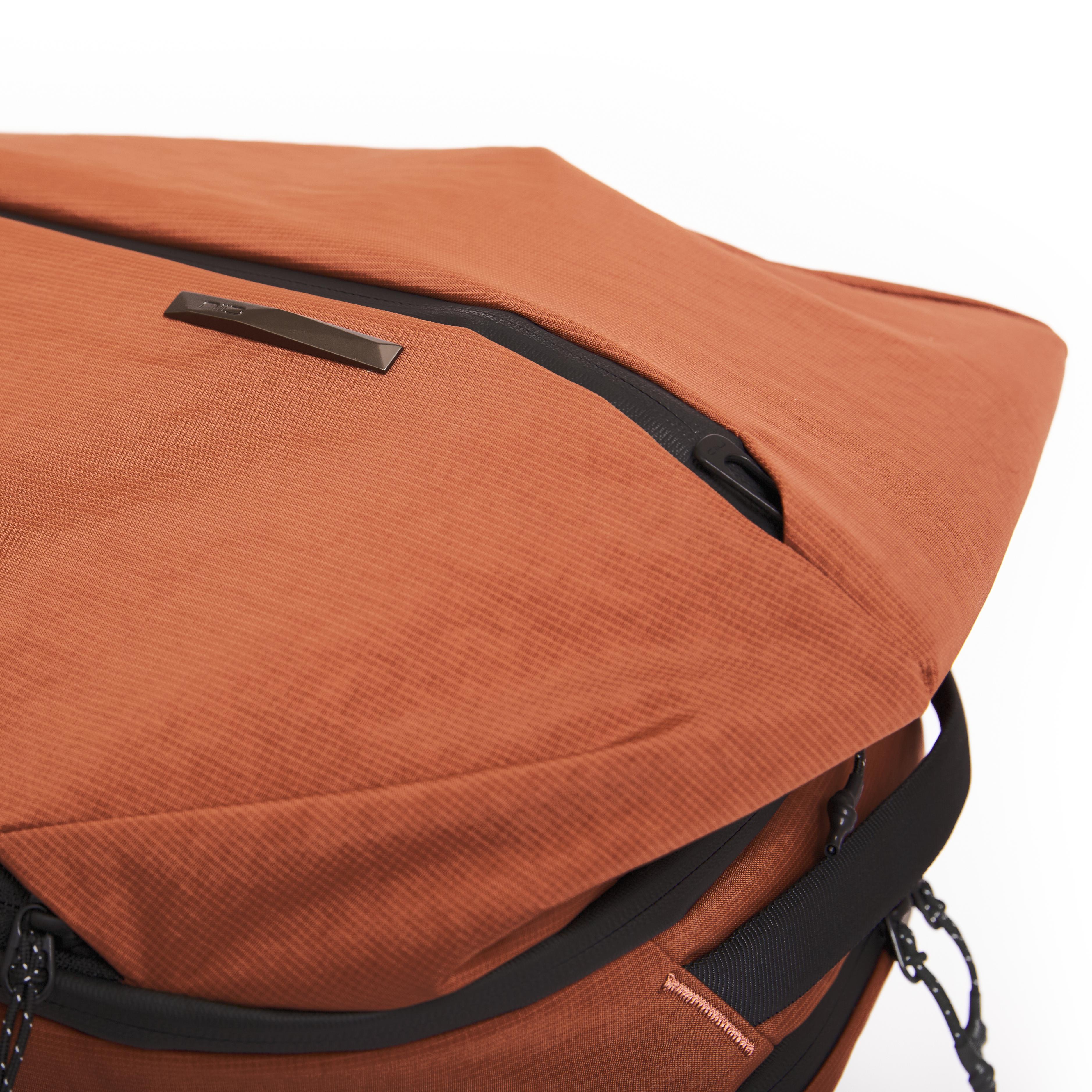 Close-up of NIID NEO Nomad Backpack N4 in Venetian Red, diagonal zipper and NIID metal logo plate on textured fabric.