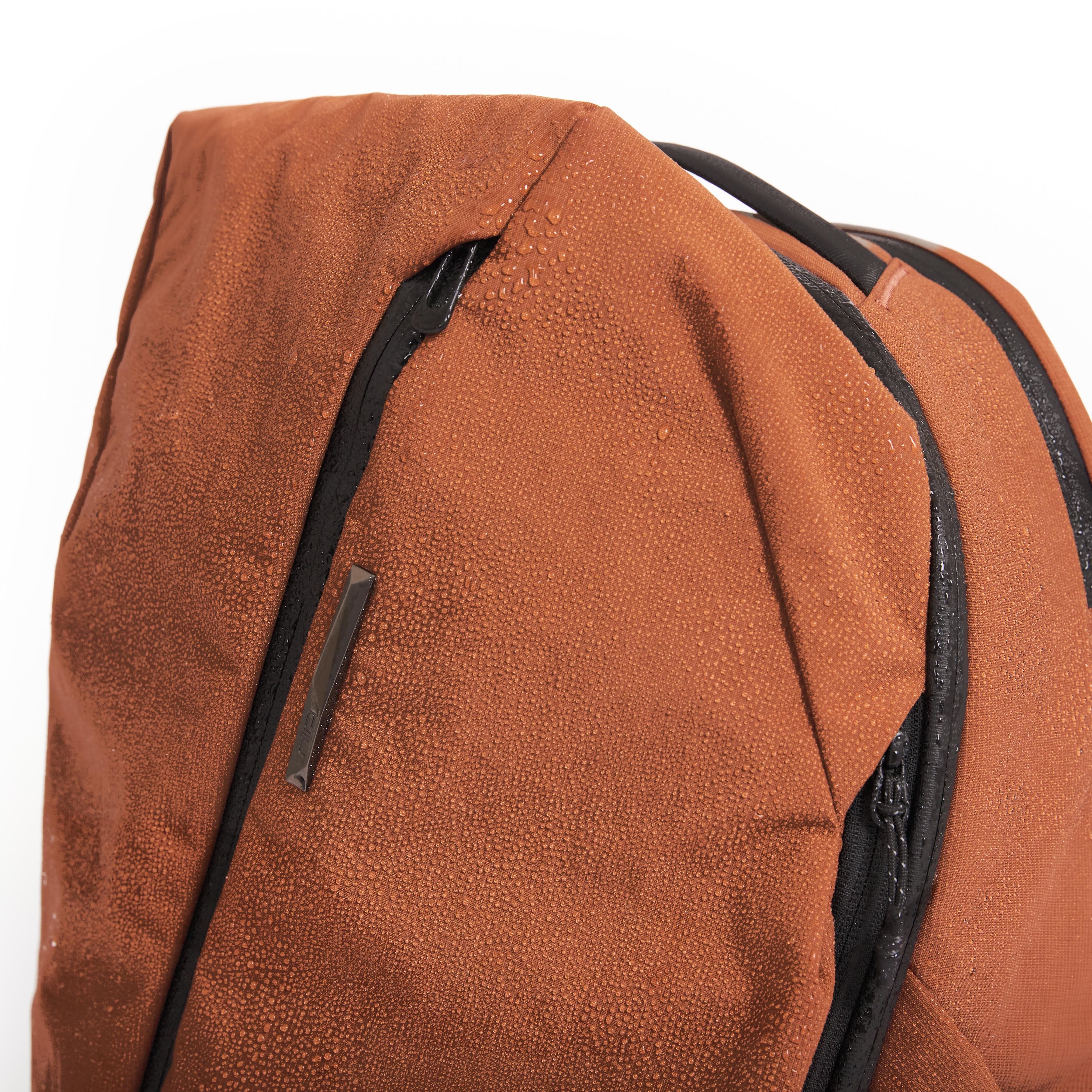 Close-up of NIID NEO Nomad Backpack N4 in Venetian Red water-repellent fabric with water droplets beading on surface.