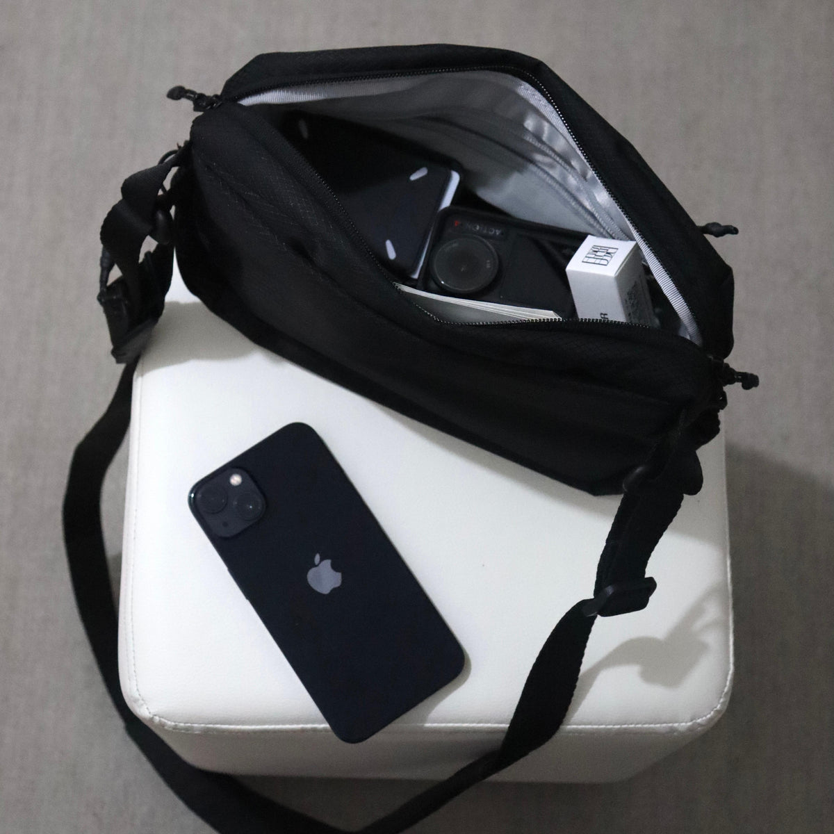 NIID NEO Nomad 4L Sling Bag‑N1 diamond grid black sling bag top‑down shot, open interior showing storage capacity, camera and small gadgets inside, smartphone placed beside bag, neutral indoor scene