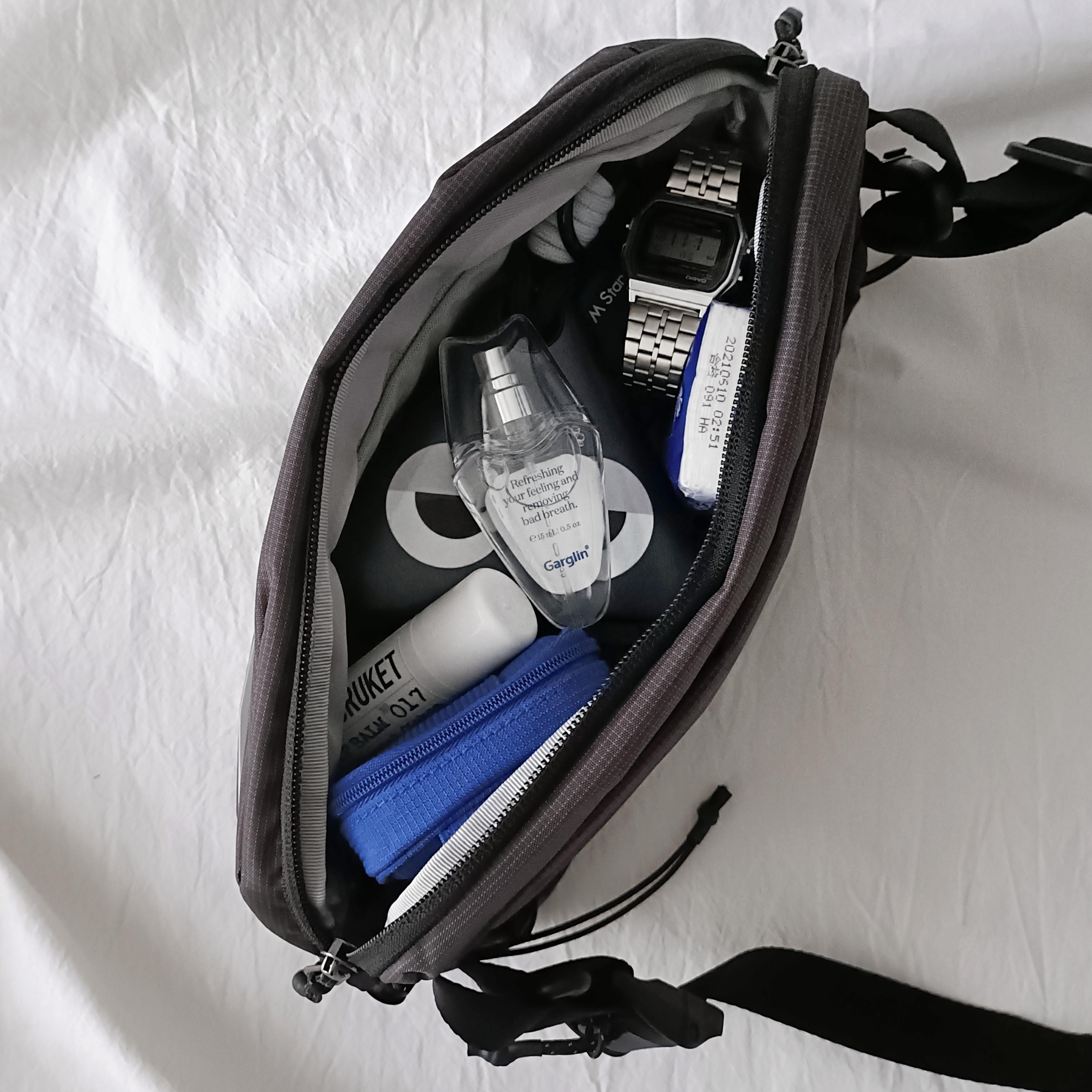 NIID NEO Nomad 4L Sling Bag‑N1 graphite gray sling bag top‑down open interior view, packed with watch, perfume and daily EDC essentials, laid on soft white fabric background