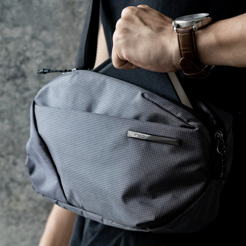 NIID NEO Nomad 4L Sling Bag‑N1 Graphite Gray unisex waterproof lightweight crossbody sling bag, close‑up view of metal NIID logo plate and grid fabric texture, 4L EDC chest bag