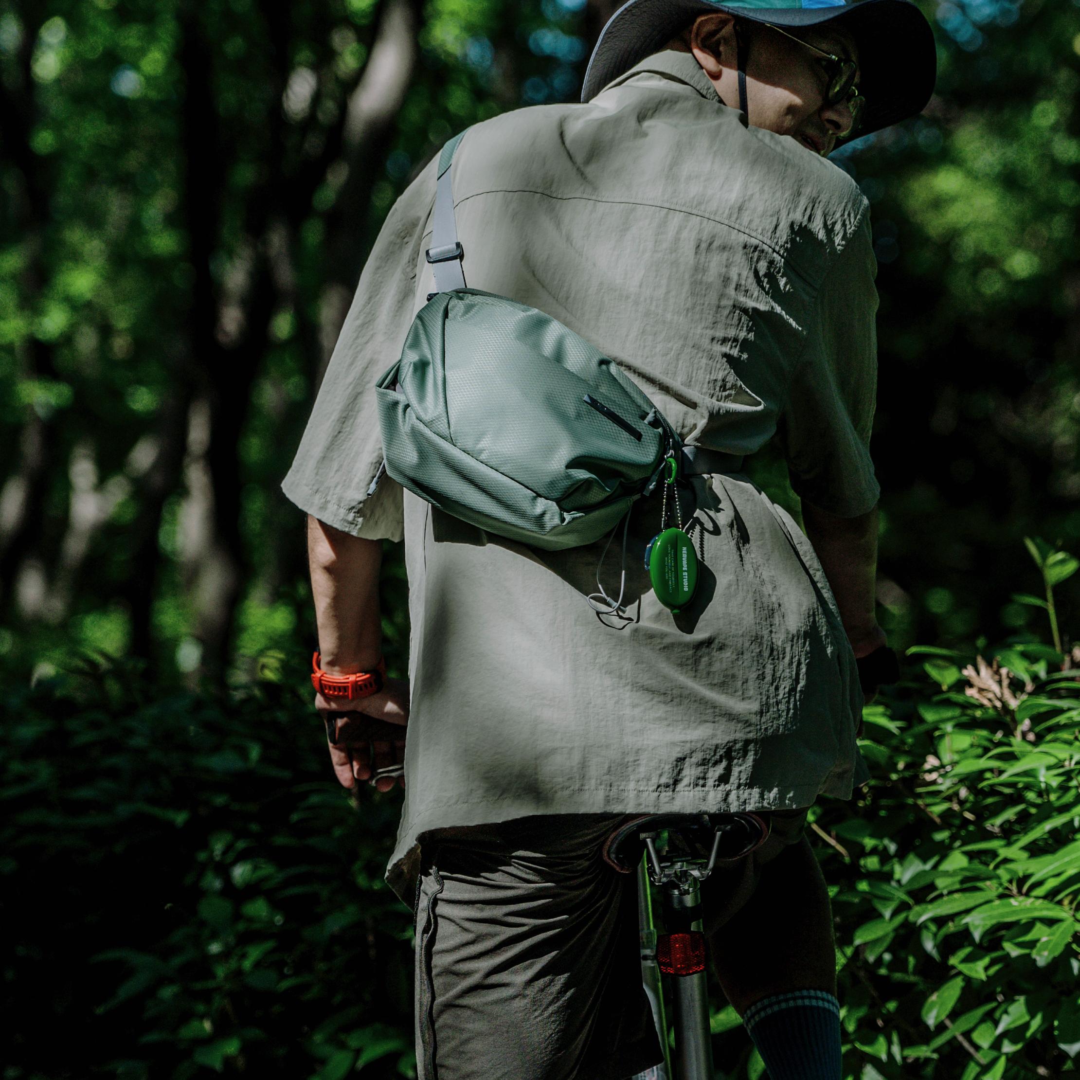 NIID NEO Nomad 4L Sling Bag‑N1 sage green diamond grid sling bag back view, man riding bicycle in green forest woods, outdoor hiking cycling EDC crossbody bag