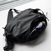 Side view of NIID NEO Nomad 5L Sling Bag‑N1L black, expandable mesh side pocket holding plastic water bottle, demonstrate flexible storage capacity for outdoor commute.