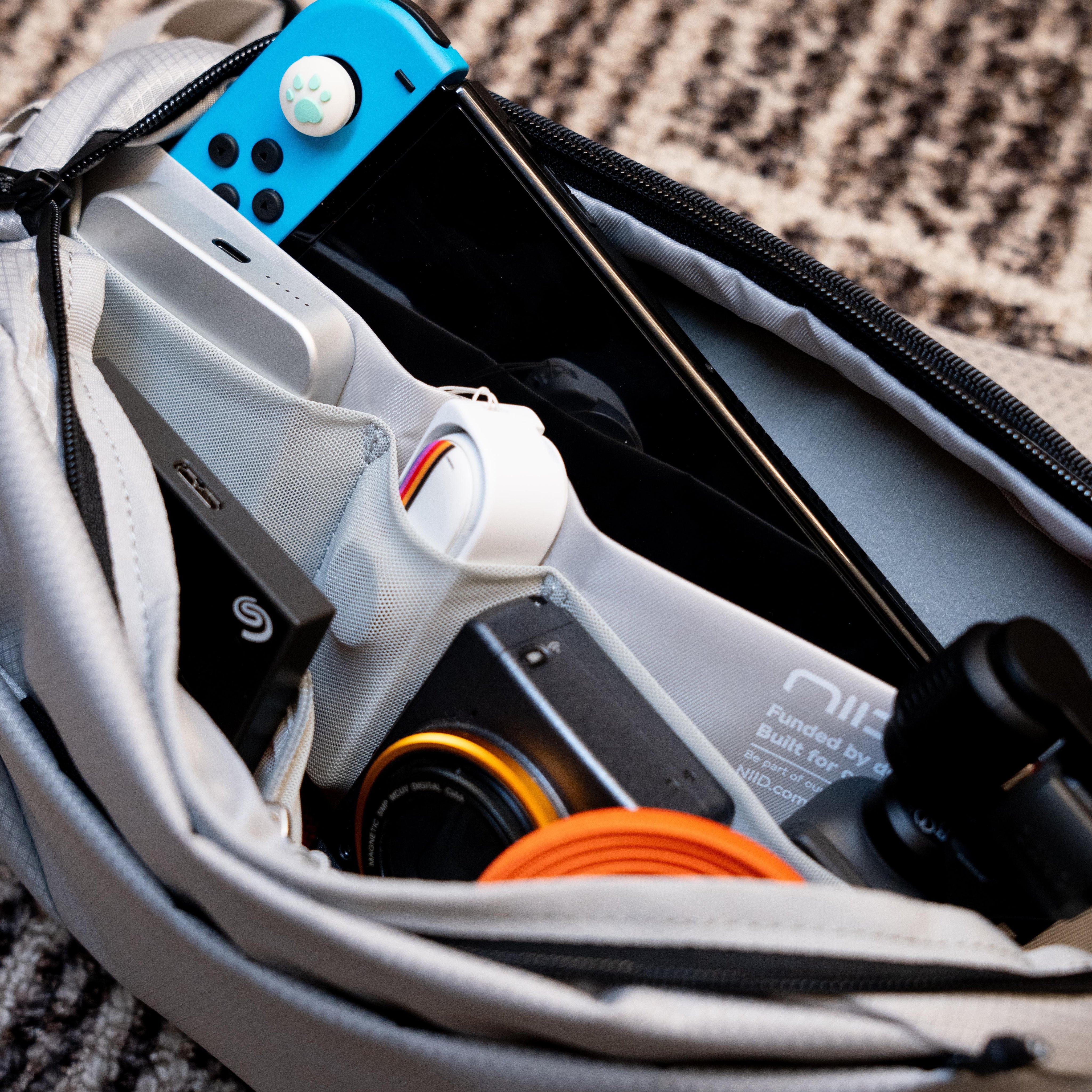 Open‑bag interior shot of NIID NEO Nomad 5L Sling Bag‑N1L, multi‑compartment packed with Nintendo Switch, camera lens, power bank and cables, showcase versatile EDC storage for travel and gaming.