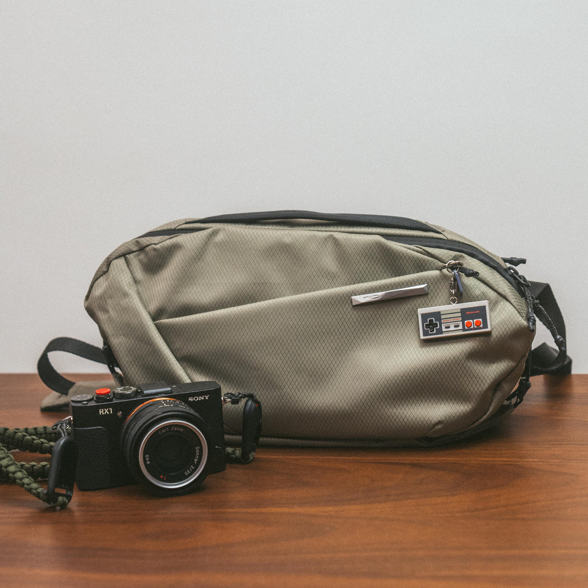 Flat‑lay table shot of NIID NEO Nomad 5L Sling Bag‑N1L pearly gray textured crossbody bag, placed beside compact Sony camera on wooden table, everyday EDC travel gear display.