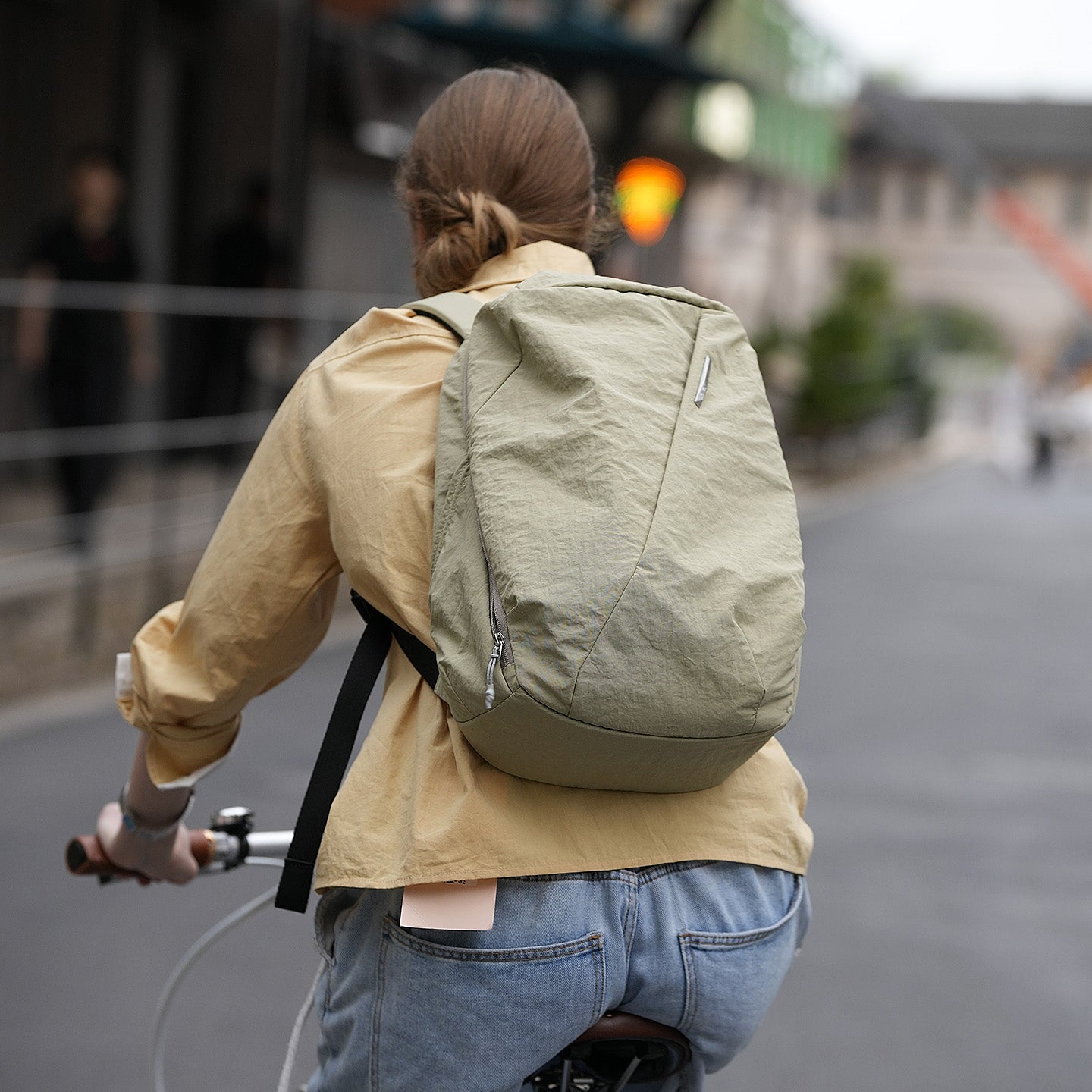 Woman riding bicycle outdoors with sage‑green NIID NEO Nomad Backpack‑N3