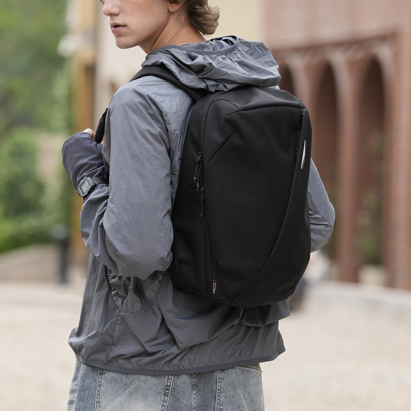 Young man outdoors wearing black NIID NEO Nomad N3 backpack, casual hooded jacket and jeans