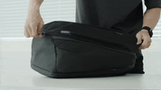 Person unzipping FortiTex Black Cordura Nomad Backpack on table, showing main compartment opening and #FortiTex tag.