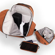 Venetian Red Nomad Backpack open with laptop and clothes, Tech Pouch with smartwatch and cable, Element Pouch with passport and ticket, travel packing shot.