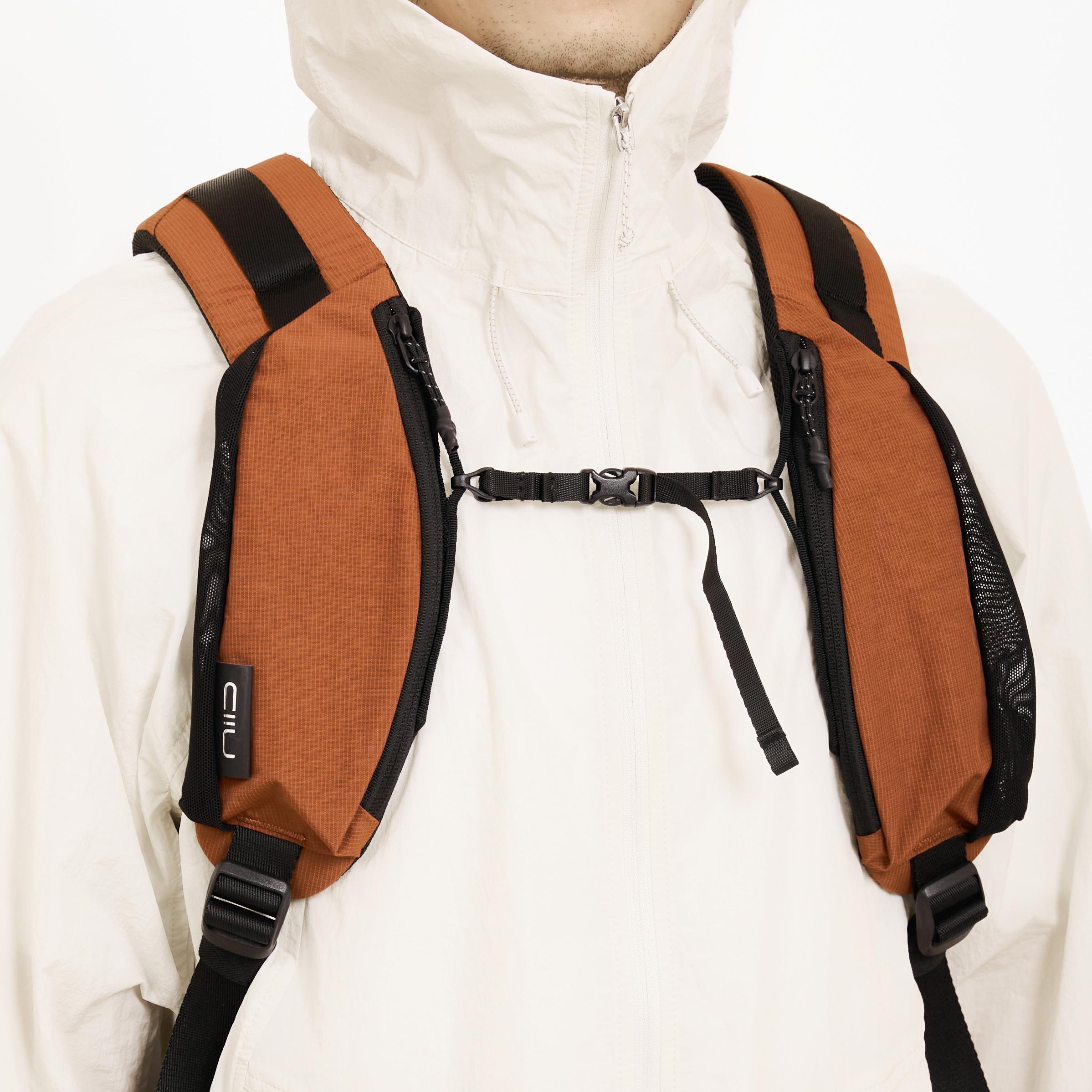 Close-up of Venetian Red backpack shoulder straps with sternum buckle worn over white jacket, showing NIID logo tag and padded mesh.