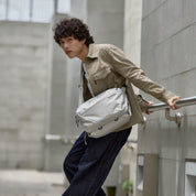 Male model carrying NIID N2 pearly gray sling bag, outdoor city street fashion photo