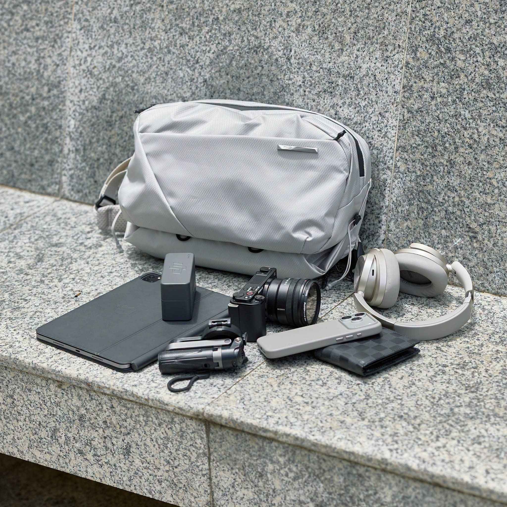 NIID N2 pearly gray sling bag with daily travel gadgets flat lay shot on stone bench