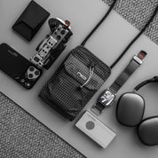 Flat lay of black diamond grid black NIID NEO Nomad Pouch with camera, phone, watch and headphones, lightweight crossbody pouch for tech gadgets
