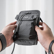 Close-up of hands holding black diamond grid NIID NEO Nomad Pouch, showing NIID logo and magnetic drawstring clasp, lightweight crossbody travel pouch.